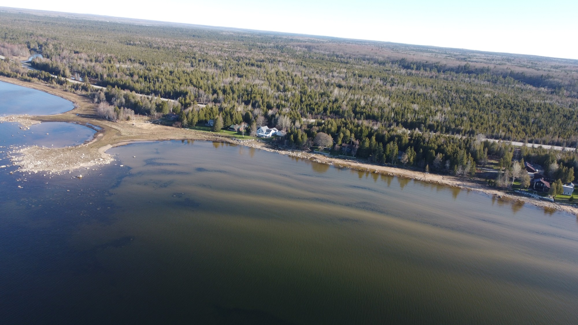 Wide aerial view of shoreline, trees, homes, and water